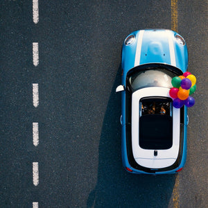 Blue car driving on a road with colourful balloons.