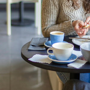 Coffee cups sitting on a table in a cafe with person.