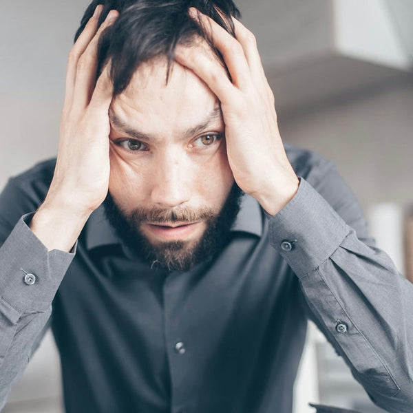 Man in grey shirt with hands on head in frustration.