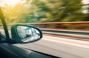View of side mirror on vehicle while driving fast down a roadway.