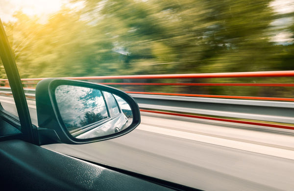 View of side mirror on vehicle while driving fast down a roadway.