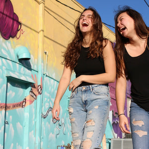Two young women laughing and walking in front of a colourful mural, showcasing a vibrant street art scene, reflecting the fun and adventurous spirit of Mystery Day Trips in Ontario.