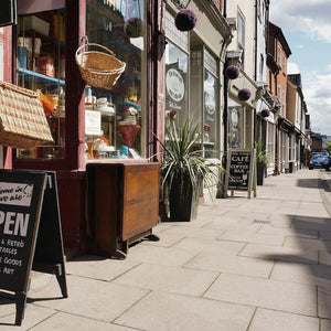 Street view of a quaint shop with vintage furniture and signs on a sunny day.