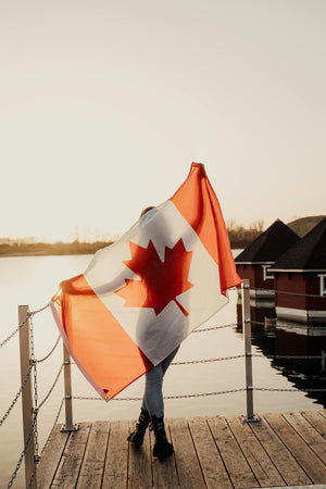 Person holding a Canadian flag on a wooden dock by a body of water. Representing Mystery Day Trips as 100% Canadian owned and operated.