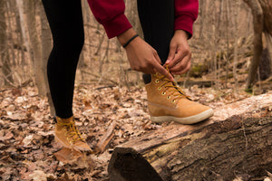 Woman tying up hiking boots on a log in the forest exploring Ontario on a Mystery Day Trip.